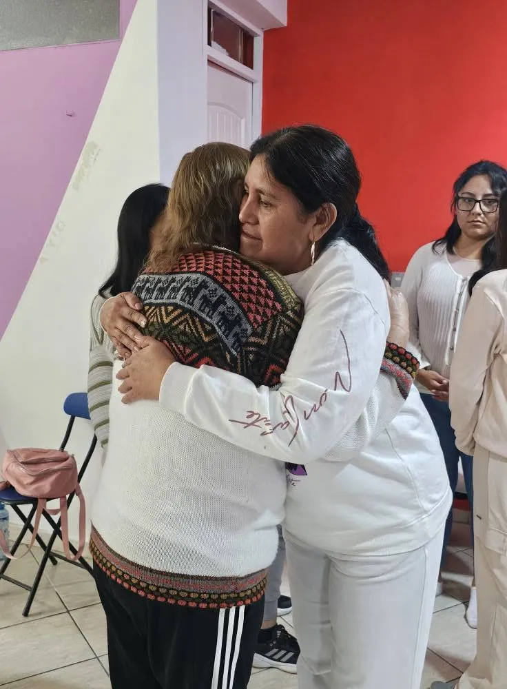 Dos participantes comparten un abrazo durante un encuentro de INHOA